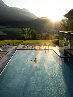 Luftaufnahme des Infinity-Pools, in dem eine Person schwimmt, bei Sonnenuntergang.