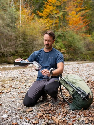 Ein Mann, Matthias Breitsameter, der das Yoga-, Wein- und Genuss-Retreat durchführt, kniet im Wald und schenkt gerade ein Glas Wein ein.