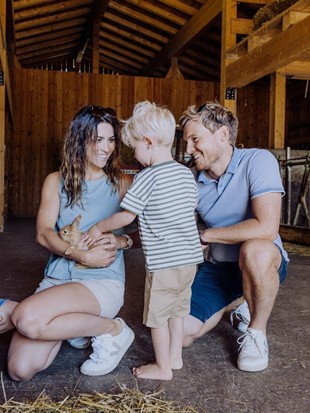 Zwei Erwachsene und zwei Kinder hocken im Bio-Bauernhof und heben und streicheln einen Hasen. 