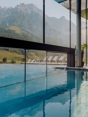Infinity-Pool von innen mit Glasfront und Blick auf die Bergkulisse im Sommer.