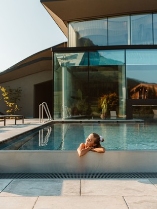 A woman is leaning on the edge of the outdoor infinity pool, enjoying the sun on her face.