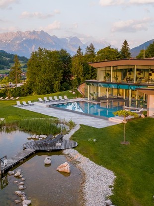 Infinity pool and natural swimming pond in summer, surrounded by green meadows.