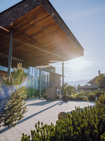 Haupteingang des Naturresorts Puradies in Leogang im Sommer, mit Vorplatz und grünen Stauden im Vordergrund.