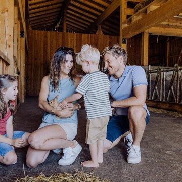 Zwei Erwachsene und zwei Kinder hocken im Bio-Bauernhof und heben und streicheln einen Hasen. 