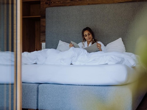 Frau liegt gemütlich im Bett und liest ein Magazin im Zimmer des Naturresort Puradies in Leogang.
