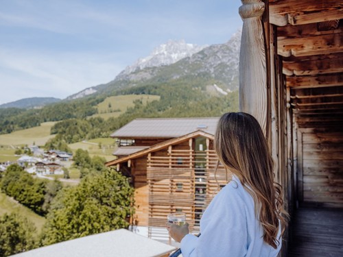 Frau im Bademantel blickt vom Balkon auf das Tal und die Berge von Leogang im Naturresort Puradies.