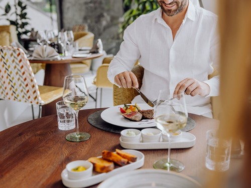 Gast genießt ein angerichtetes Fleischgericht mit Weißwein im Restaurant des Naturresort Puradies.