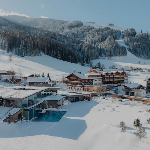 Luftaufnahme des Naturresorts Puradies in Leogang im Winter, mit schneebedeckten Wiesen und der gesamten Anlage inmitten einer winterlichen Landschaft.