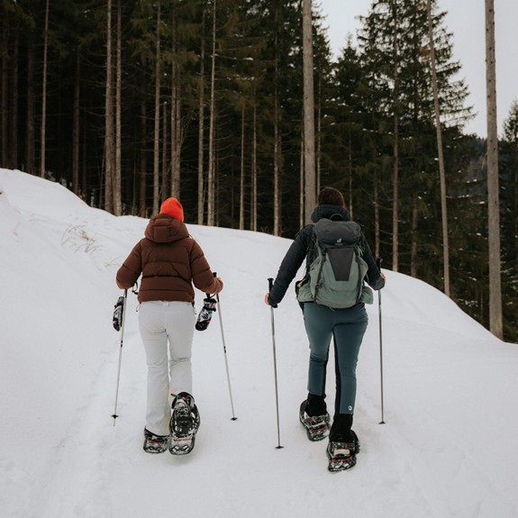 Zwei Personen wandern mit Schneeschuhen durch eine verschneite Winterlandschaft, umgeben von schneebedeckten Bäumen.