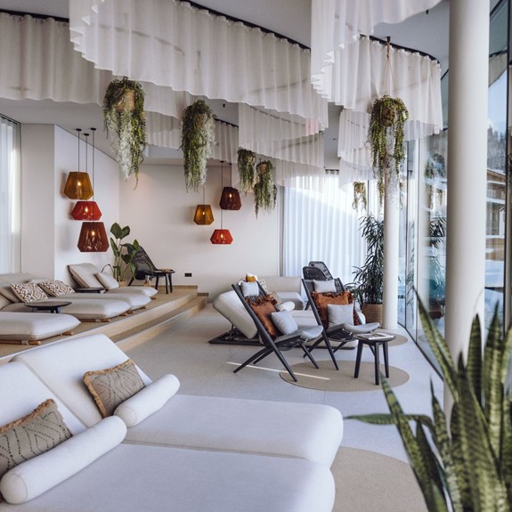 Ruheraum Heaven Spa mit Glasfront, im Winter, schneebedeckt, mit Blick auf den Hotelgarten, das Badhaus und einen Teil des Hotels.