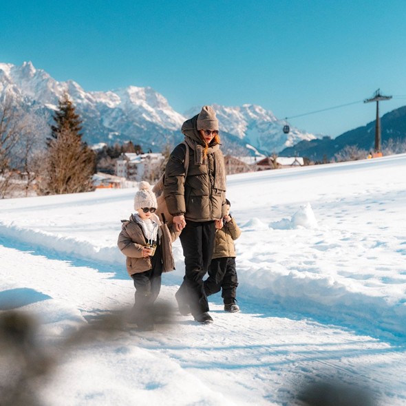 A woman walks hand in hand with two small children through a snowy winter landscape.