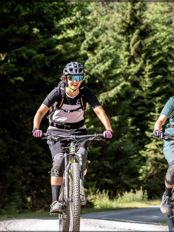 Zwei lachende Mountainbikerinnen fahren auf einem Forstweg im Wald bei Leogang