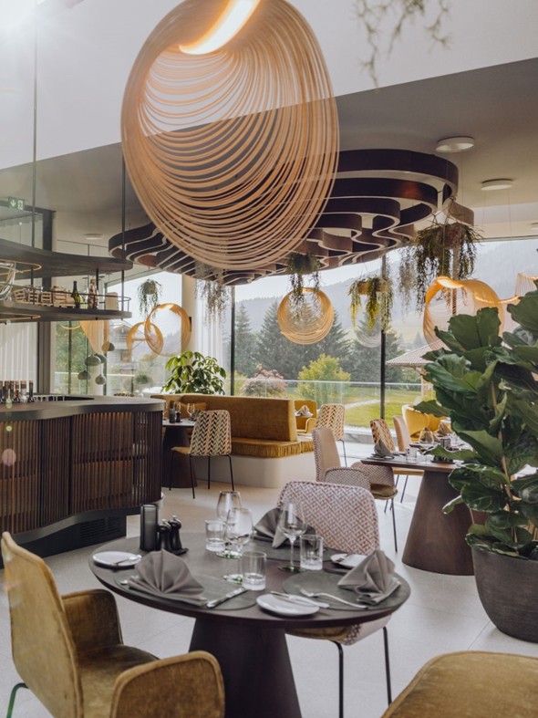 Schön gedeckte Tische im Gourmetrestaurant Essenz, mit Front-Cooking-Küche und einer Glasfront, die einen Blick auf die sommerliche Landschaft freigibt.